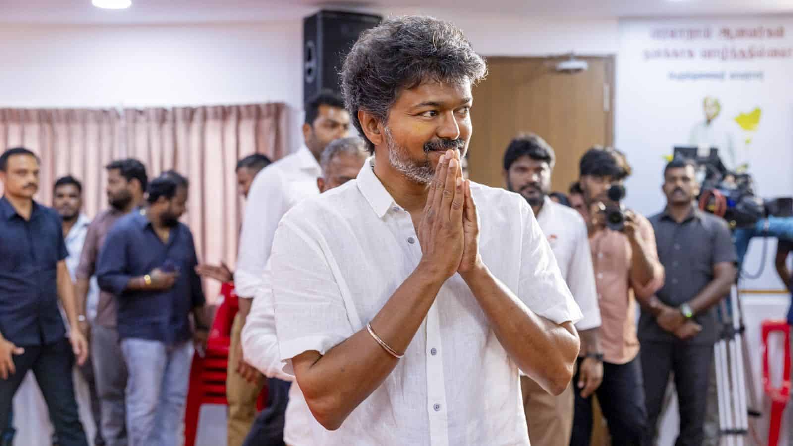 Man with folded hands at election results event, surrounded by media and supporters in Kerala.