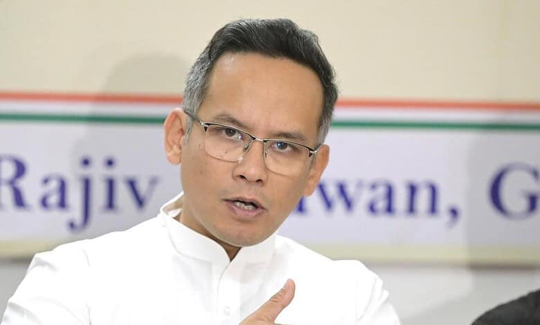 Politician speaking at a meeting about Assam election performance, wearing glasses and white attire.