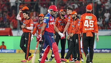 Cricket team celebrating during a match with players in orange and blue uniforms.