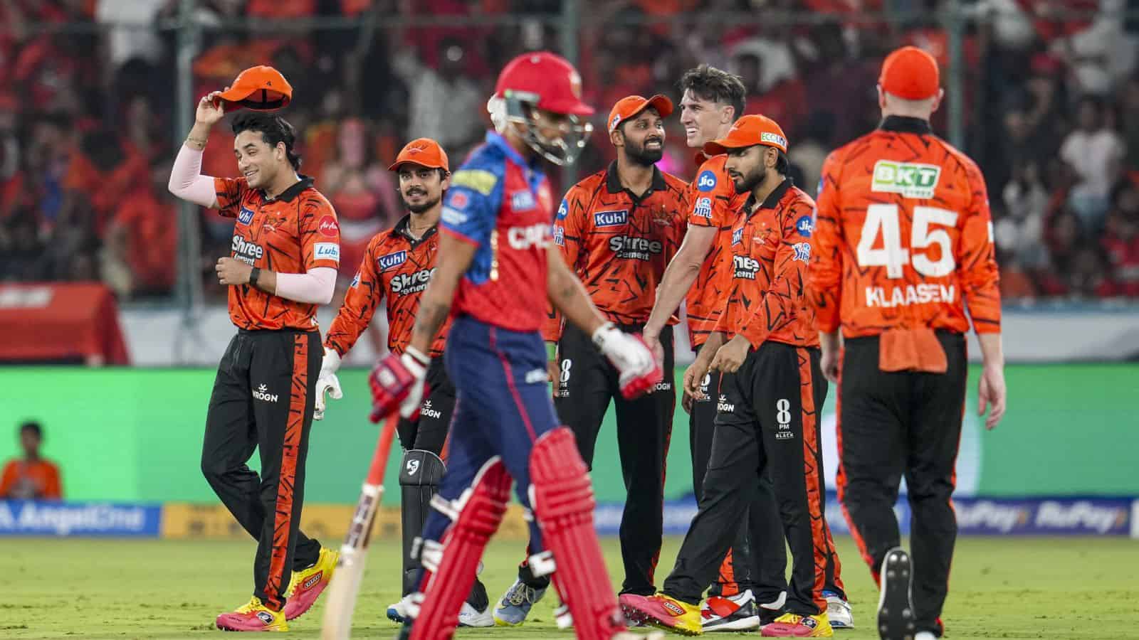 Cricket team celebrating during a match with players in orange and blue uniforms.