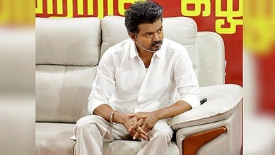 A man in a white shirt sitting on a beige sofa during a political meeting or discussion.