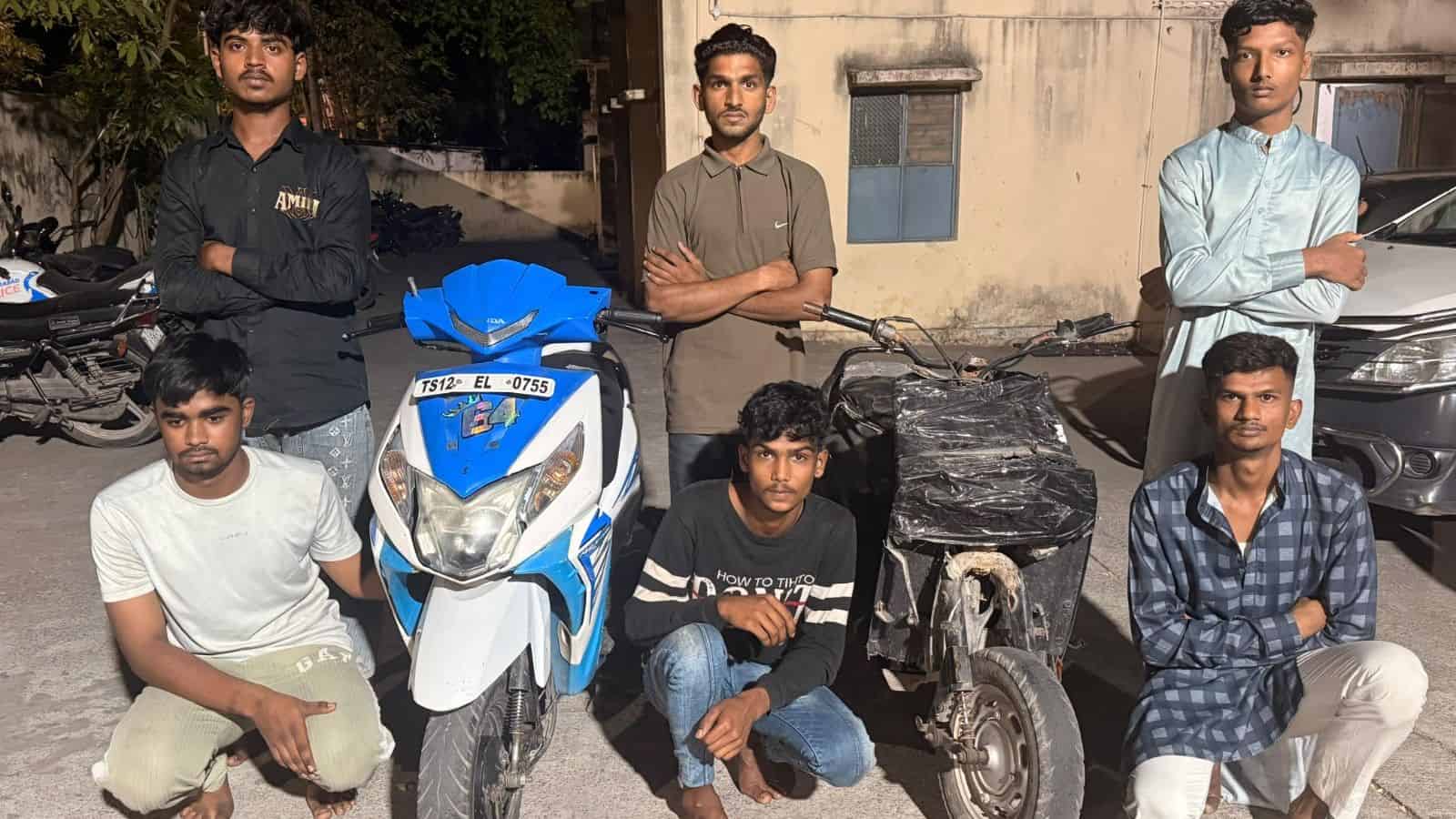 Young men standing with bikes and scooters on a street in Hyderabad, involved in illegal bike stunts.