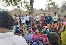 A mother and daughter with a group of women and children outdoors in a rural setting.