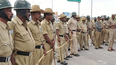 Police officers standing in a line during a formal event in Karnataka, wearing uniforms and hats, with so.