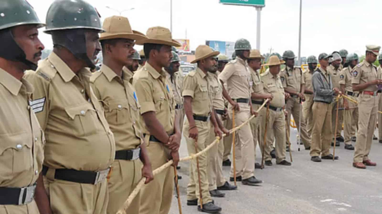 Police officers standing in a line during a formal event in Karnataka, wearing uniforms and hats, with so.