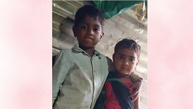 A young boy and girl standing together indoors, smiling at the camera, in a casual setting.