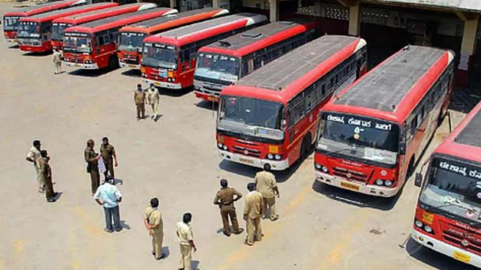 Red public buses parked in a bus depot with personnel inspecting and managing the fleet.