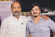 A young man and an older man standing together, smiling, with the older man’s arm around the young man’s.
