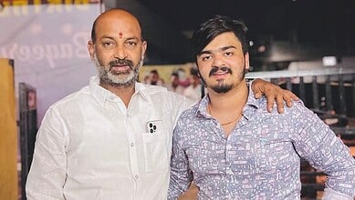 A young man and an older man standing together, smiling, with the older man’s arm around the young man’s.