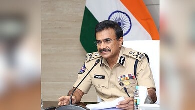 Indian police officer in uniform speaking at a press conference with the Indian flag in the background.