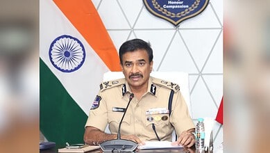 Indian police officer in uniform speaking at a desk with the Indian flag and a badge in the background.