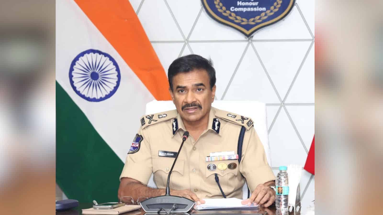 Indian police officer in uniform speaking at a desk with the Indian flag and a badge in the background.