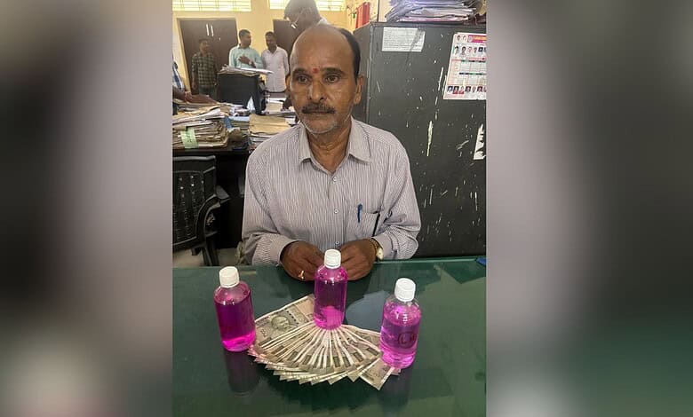 A man with a mustache sitting at a desk with three bottles of pink liquid and a fan of currency notes in.