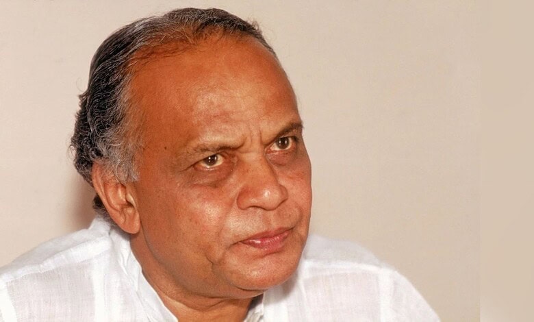 A senior man with grey hair and a serious expression, wearing a white shirt, looking to the side.
