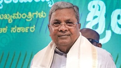 A man in traditional attire smiling at a public event with a green and blue background.