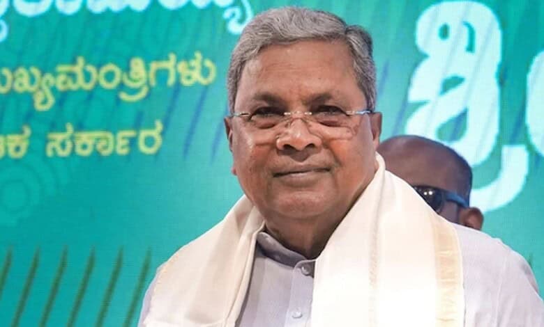 A man in traditional attire smiling at a public event with a green and blue background.