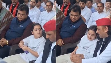 A young girl in white traditional attire sitting next to a man in a red cap and white kurta, with several.