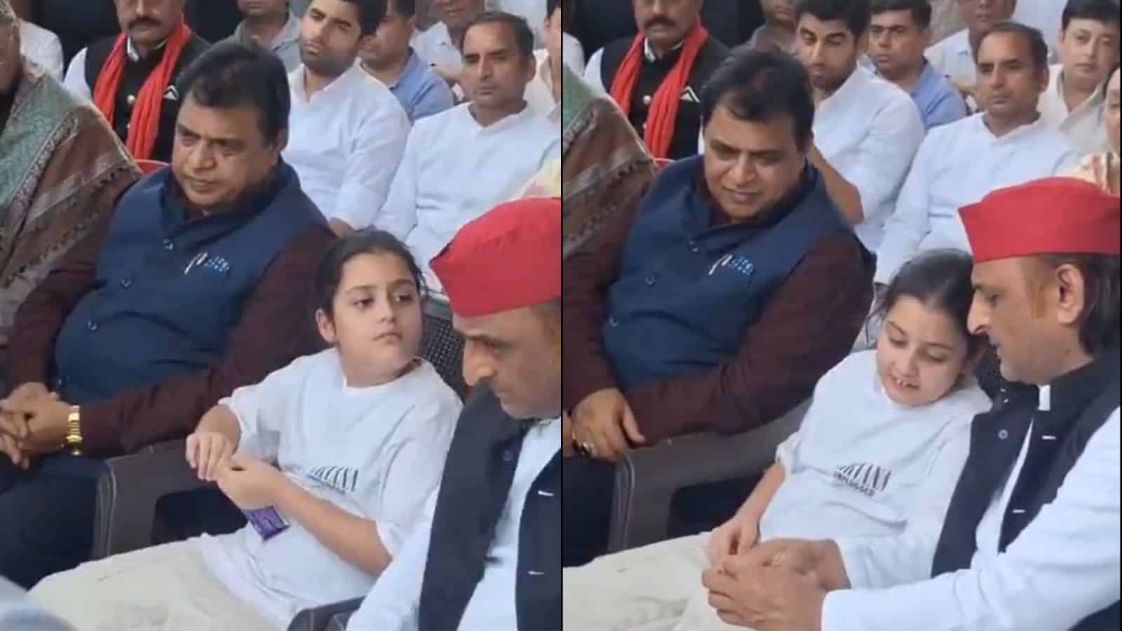 A young girl in white traditional attire sitting next to a man in a red cap and white kurta, with several.