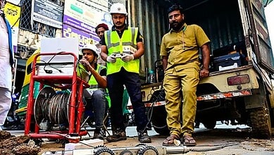 Construction workers inspecting equipment on a busy street with a cable reel and utility vehicle.