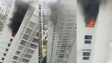 Fire and smoke emerging from a high-rise building window during a daytime fire incident.