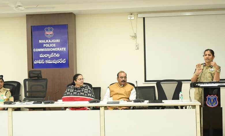 Police commissioner addressing a meeting at Malkajgiri Police Station, with officers seated at the table.