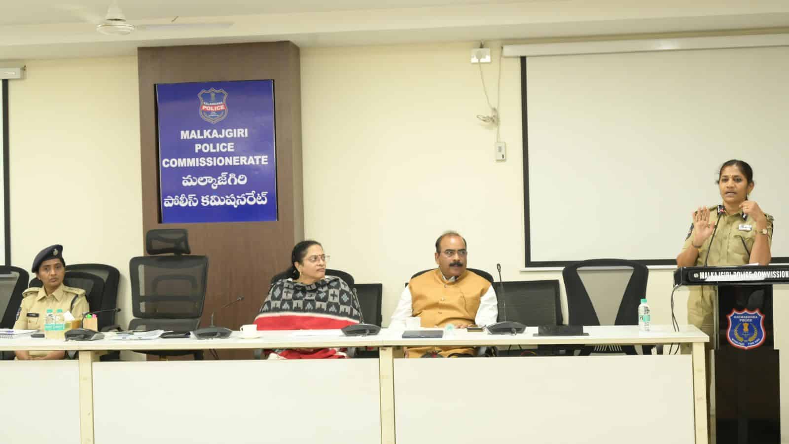 Police commissioner addressing a meeting at Malkajgiri Police Station, with officers seated at the table.