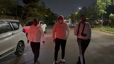 A man in a hoodie walking with two men on a street at night, illuminated by streetlights.