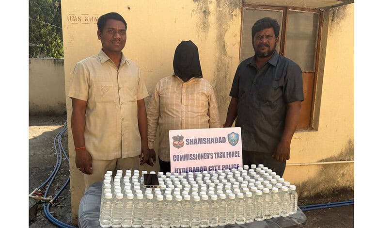A woman with her face covered standing between two men behind a table with numerous bottles of hand sanit.