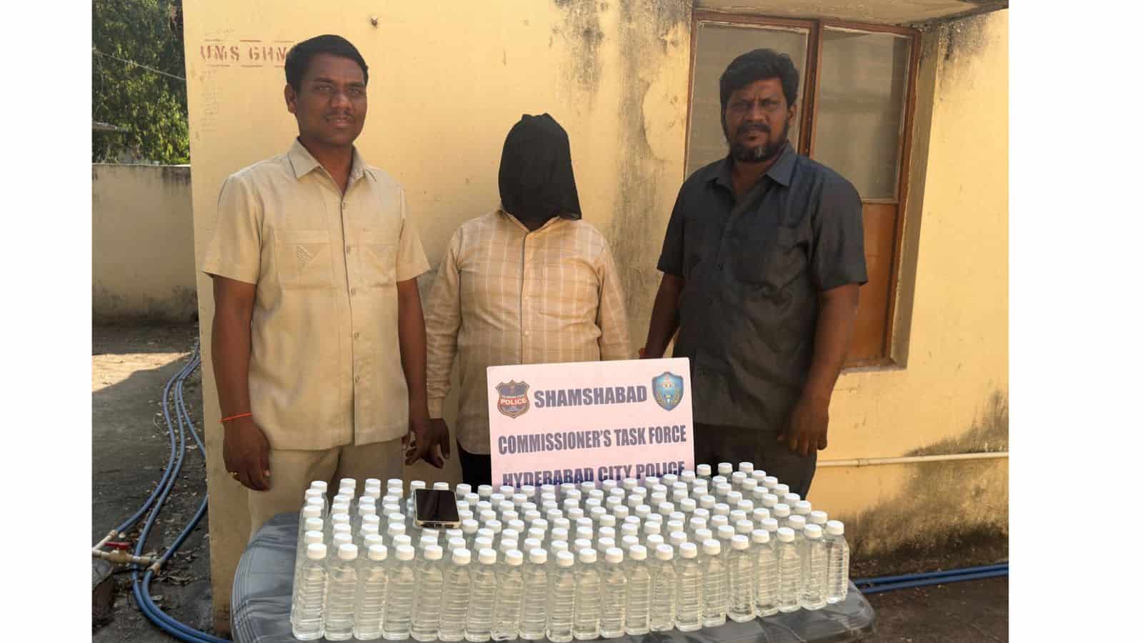 A woman with her face covered standing between two men behind a table with numerous bottles of hand sanit.