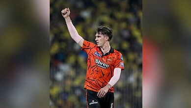 A player celebrating on the cricket field wearing an orange jersey with sponsor logos.
