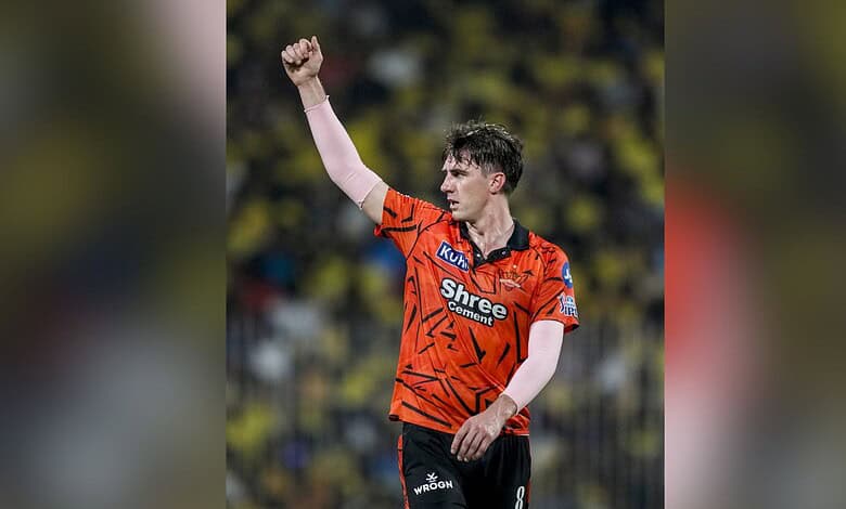 A player celebrating on the cricket field wearing an orange jersey with sponsor logos.