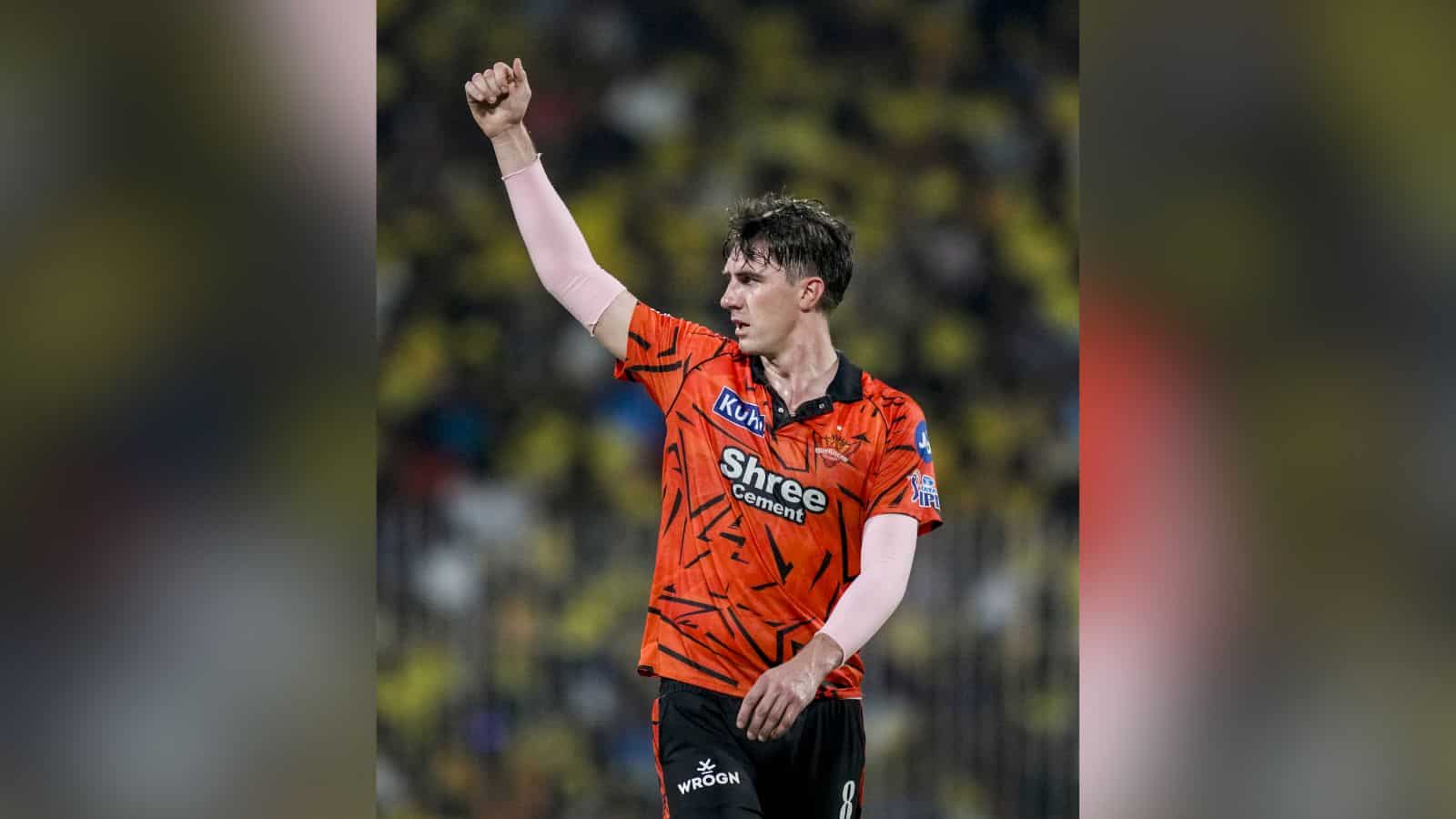 A player celebrating on the cricket field wearing an orange jersey with sponsor logos.