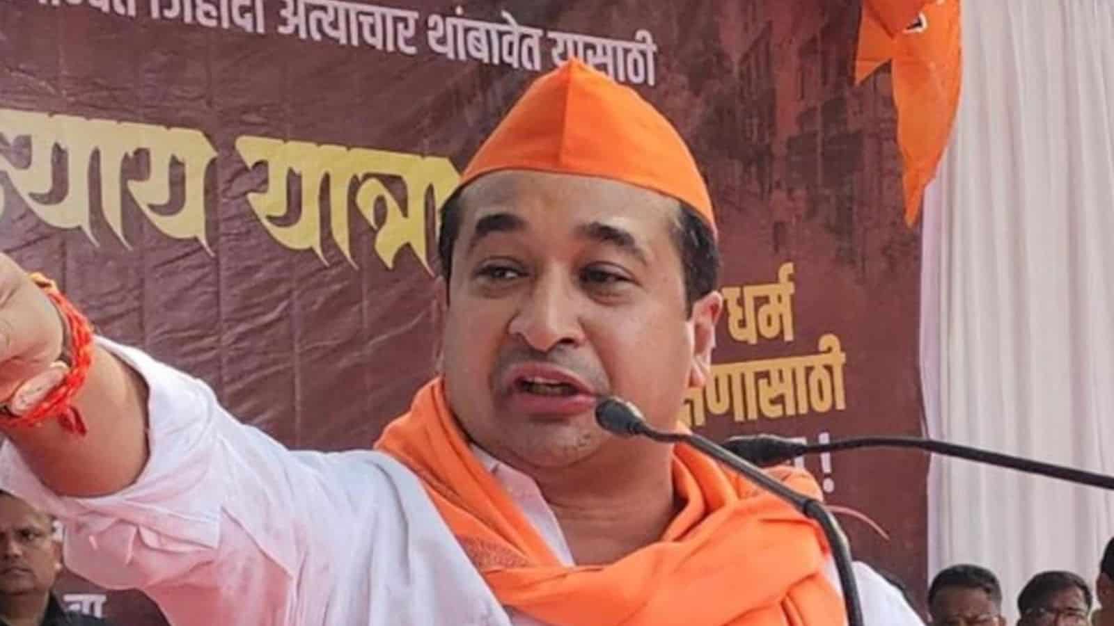 Prominent Indian politician speaking at a public event, wearing orange attire and cap, with a microphone,.