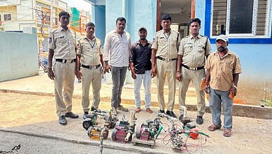 Suspected illegal water pump operators detained by police officers in front of a colourful building.