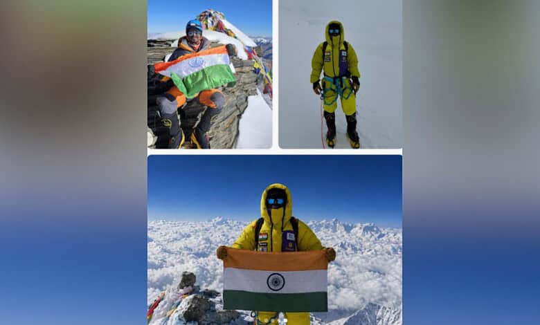 A mountaineer holding the Indian flag on a snowy peak, dressed in yellow gear with a clear blue sky backg.