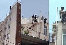 A woman and a man on a rooftop, with others assisting, in an urban setting during daytime.