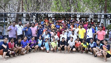 Group of young men and women posing outdoors in front of a chain-link fence, smiling and making gestures.