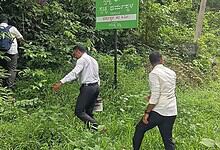 Group of men walking through dense green forest near a signboard in India.