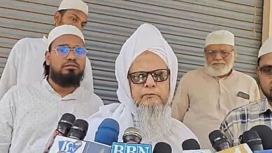 A senior Muslim cleric speaking to the media with multiple microphones in front of him.