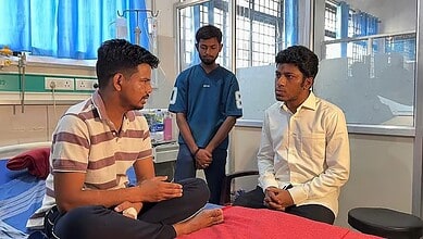 A man in a striped shirt talking to a patient in a white shirt in a hospital room, with a nurse standing.