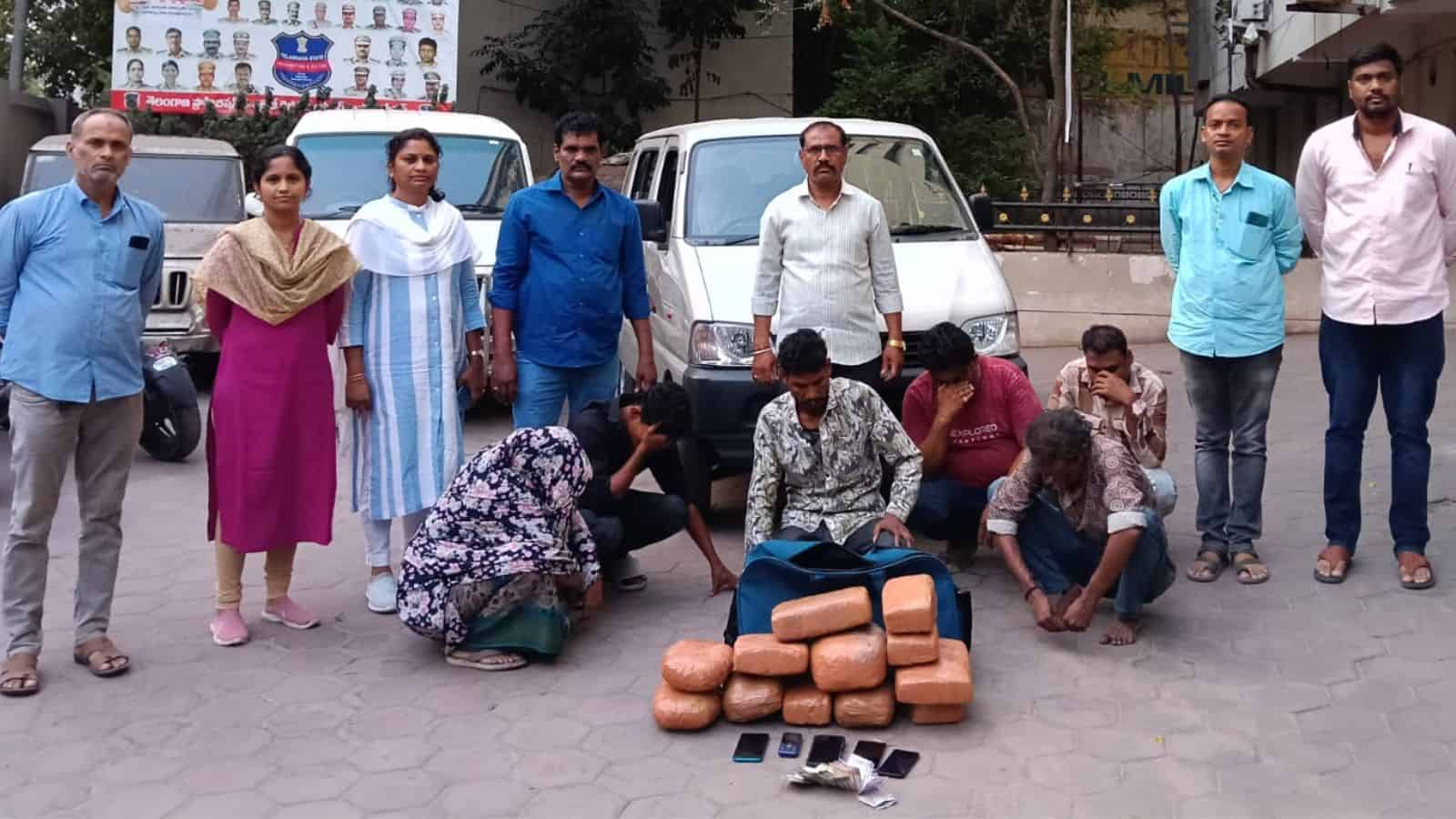 A woman and children collecting bricks on the street with men standing behind them in an urban setting.