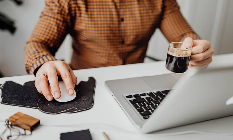 A person working on a laptop with a cup of coffee in hand at a desk.