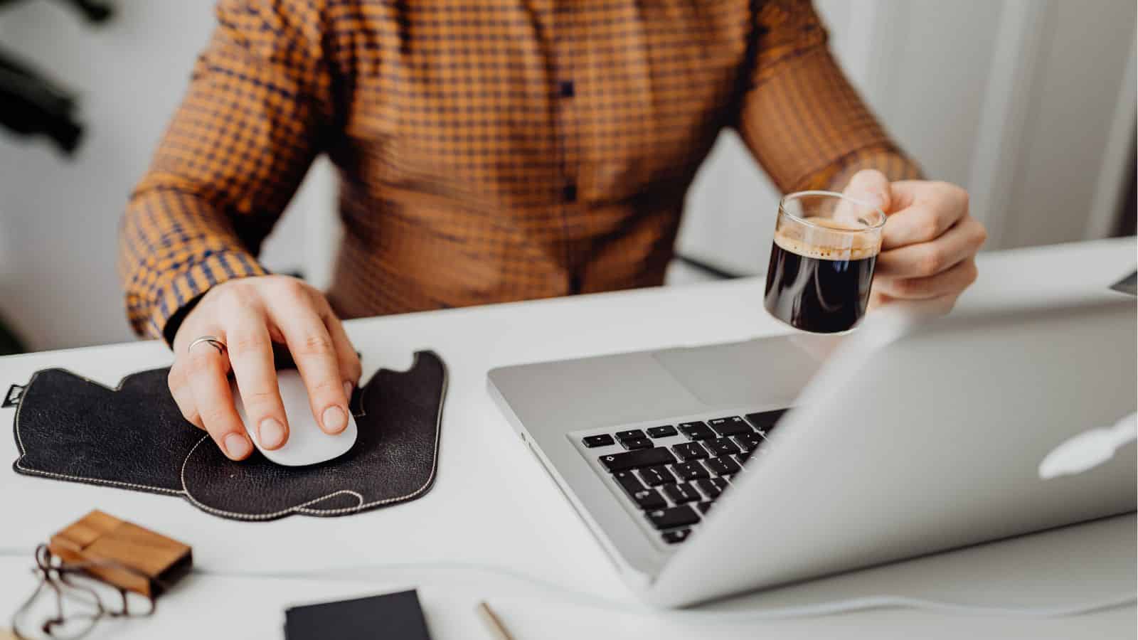 A person working on a laptop with a cup of coffee in hand at a desk.