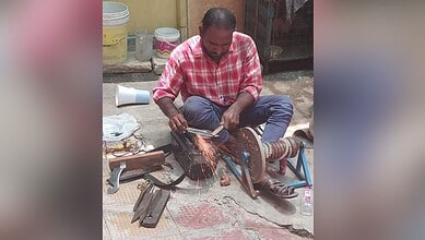 A man welding metal outdoors with sparks flying, seated on the ground, surrounded by tools and containers.
