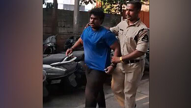 A man in a blue shirt being escorted by a police officer on a street.
