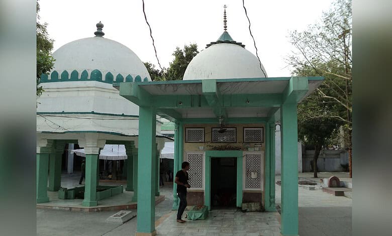 Ancient Hindu temple with domed structures and green pillars, surrounded by trees, in a peaceful outdoor.