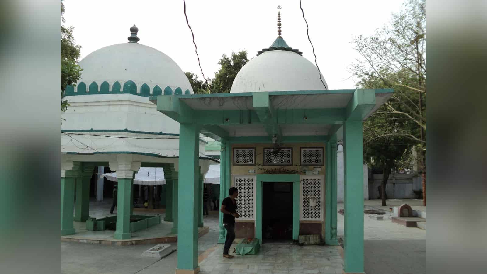 Ancient Hindu temple with domed structures and green pillars, surrounded by trees, in a peaceful outdoor.