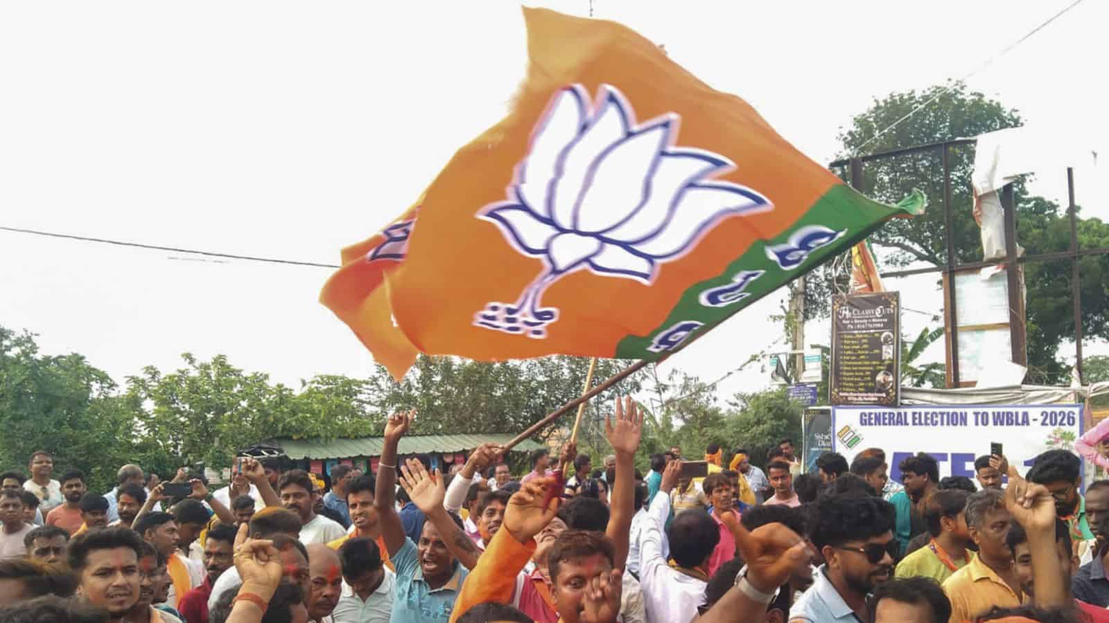 BJP party flag being waved during a political rally in India with a crowd of supporters.