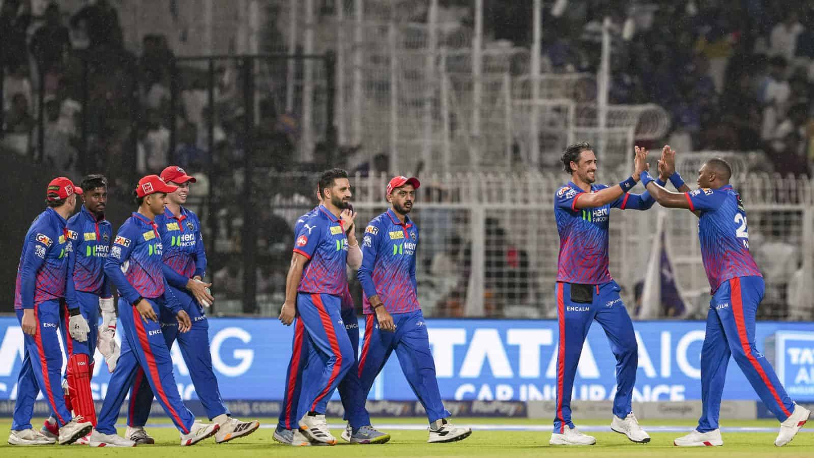 Celebrating cricket players in blue uniforms on the field during a match, with fans in the background.