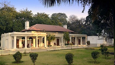 The Siasat Daily: Elegant colonial-style house with white walls, red roof, surrounded by lush greenery an.